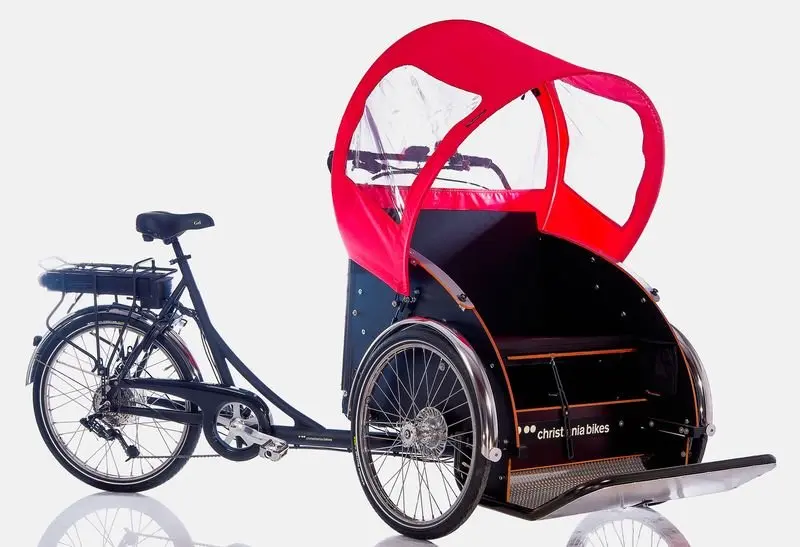 Barrierefreie Mobilität mit Stil – die Rikscha von Christiania. Christiania Rikscha mit zwei sitzenden Personen auf einem Weg im Grünen.